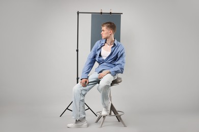 Photo of Handsome young man wearing stylish clothes sitting on chair against light grey background