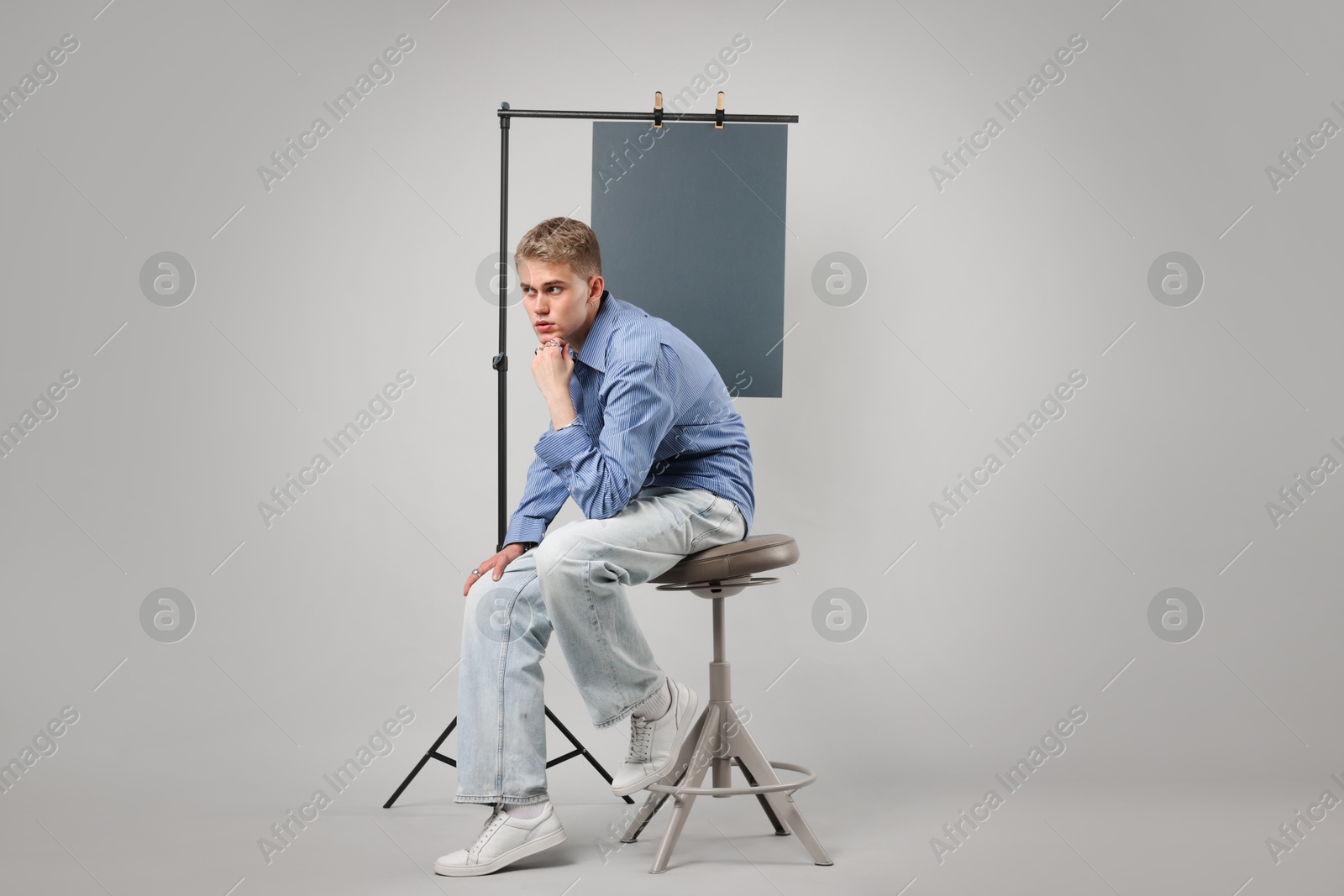 Photo of Handsome young man wearing stylish clothes sitting on chair against light grey background