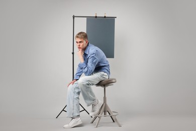 Photo of Handsome young man wearing stylish clothes sitting on chair against light grey background