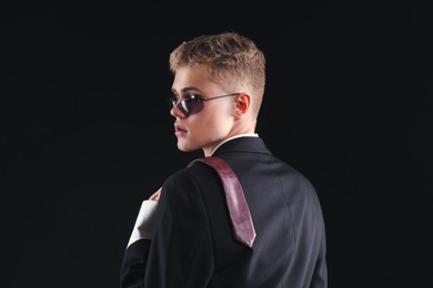 Photo of Handsome young man wearing stylish suit and sunglasses on black background