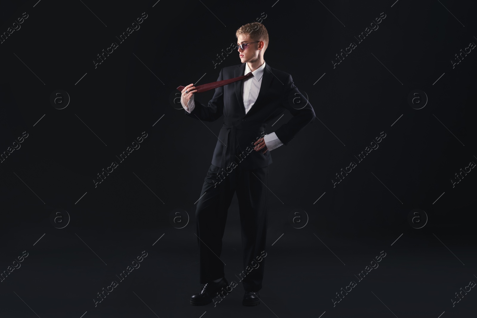 Photo of Handsome young man wearing stylish suit and sunglasses on black background