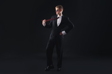 Photo of Handsome young man wearing stylish suit and sunglasses on black background