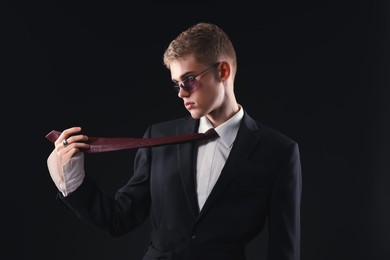 Photo of Handsome young man wearing stylish suit and sunglasses on black background