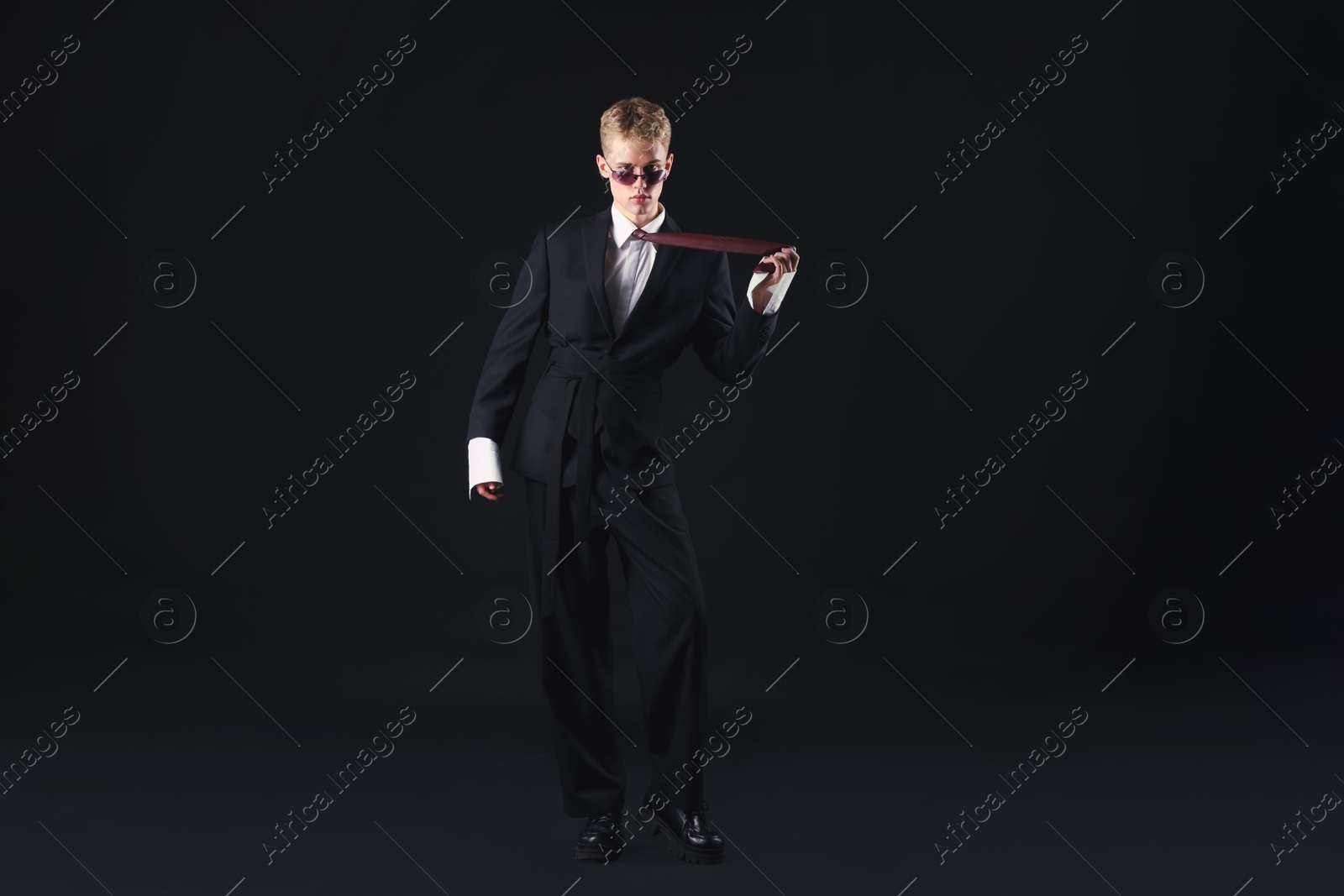 Photo of Handsome young man wearing stylish suit and sunglasses on black background