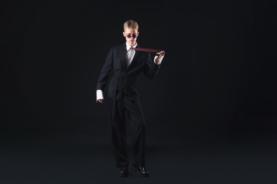 Photo of Handsome young man wearing stylish suit and sunglasses on black background