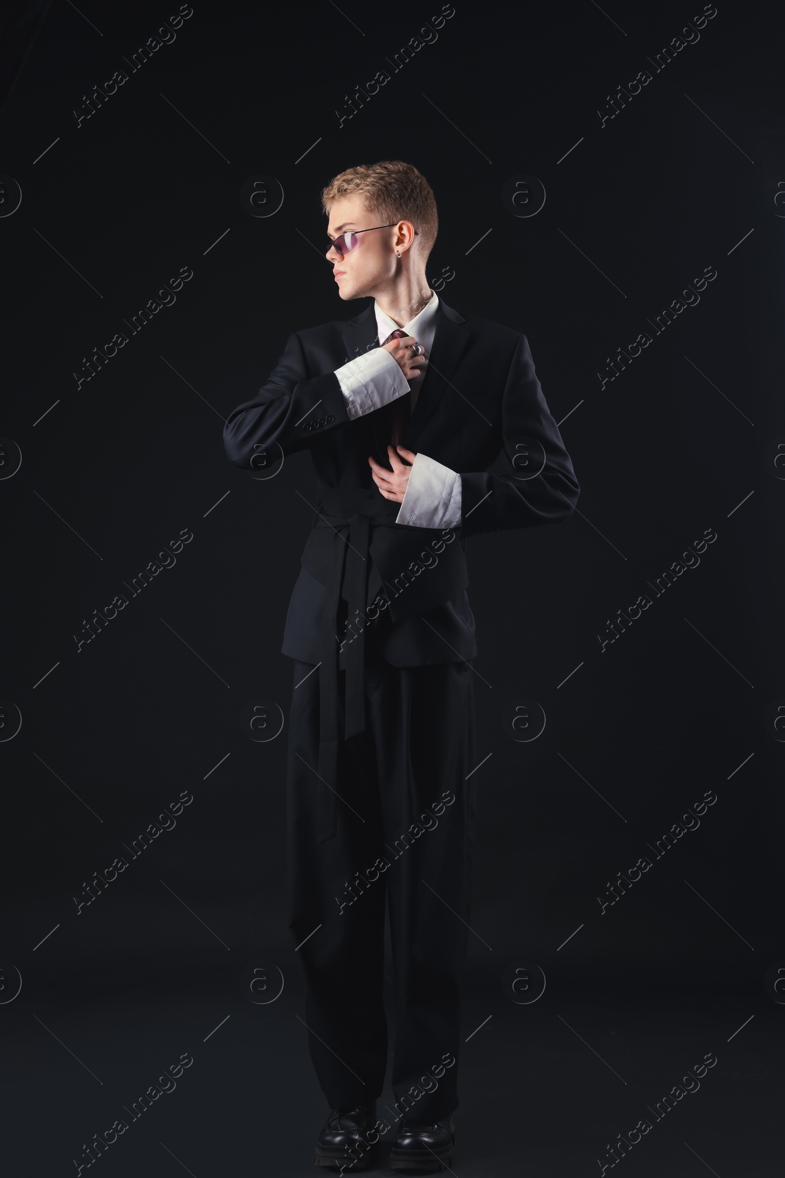 Photo of Handsome young man wearing stylish suit and sunglasses on black background