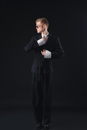 Photo of Handsome young man wearing stylish suit and sunglasses on black background