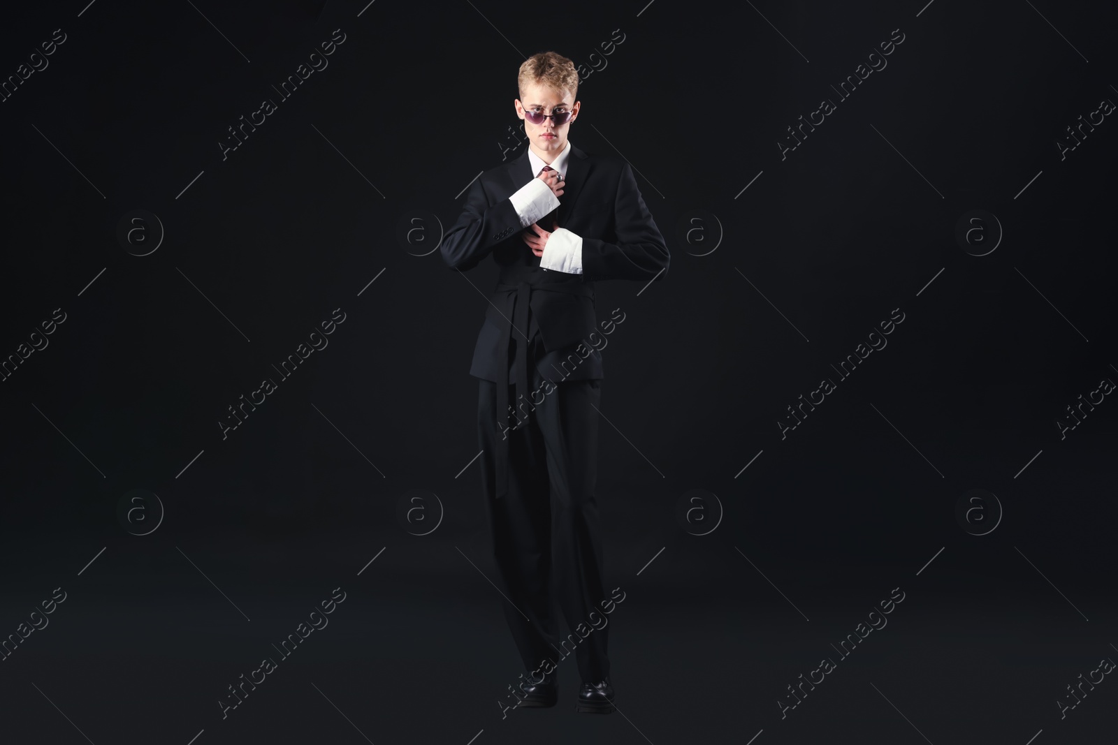 Photo of Handsome young man wearing stylish suit and sunglasses on black background