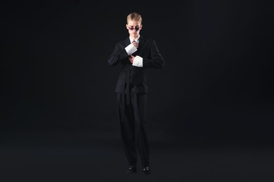 Photo of Handsome young man wearing stylish suit and sunglasses on black background