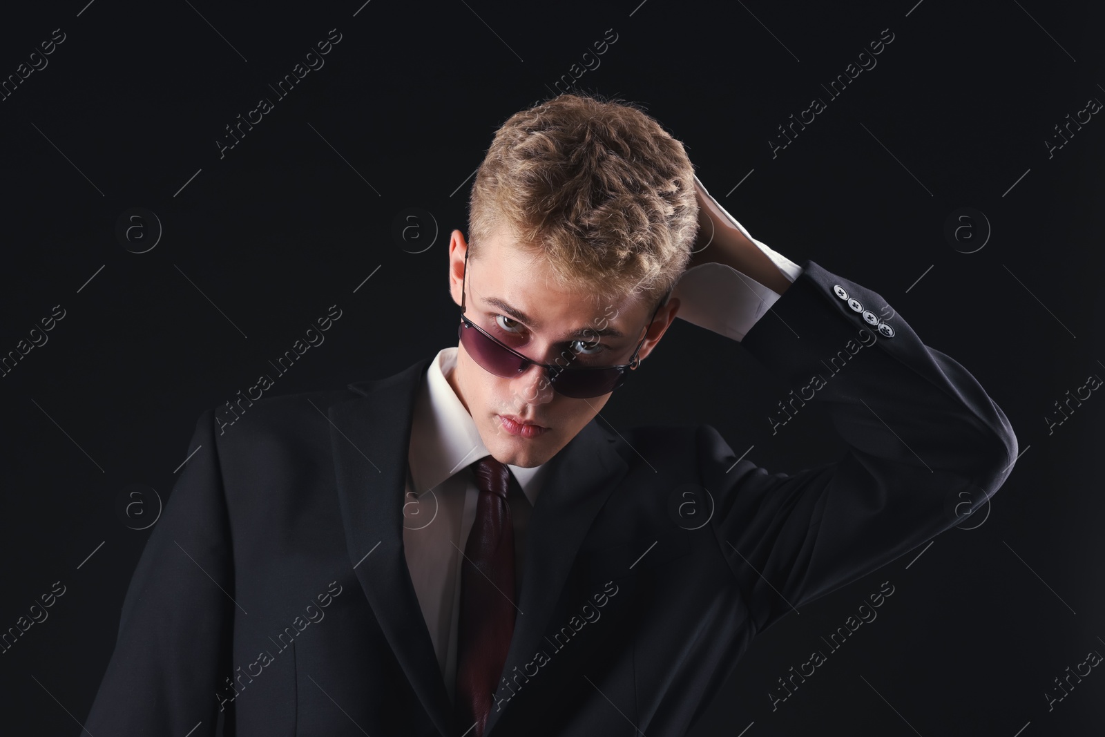 Photo of Handsome young man wearing stylish suit and sunglasses on black background