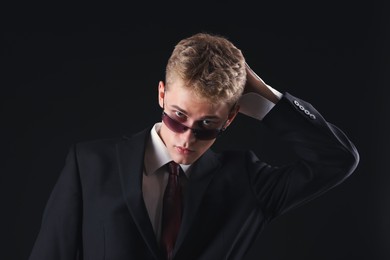 Photo of Handsome young man wearing stylish suit and sunglasses on black background