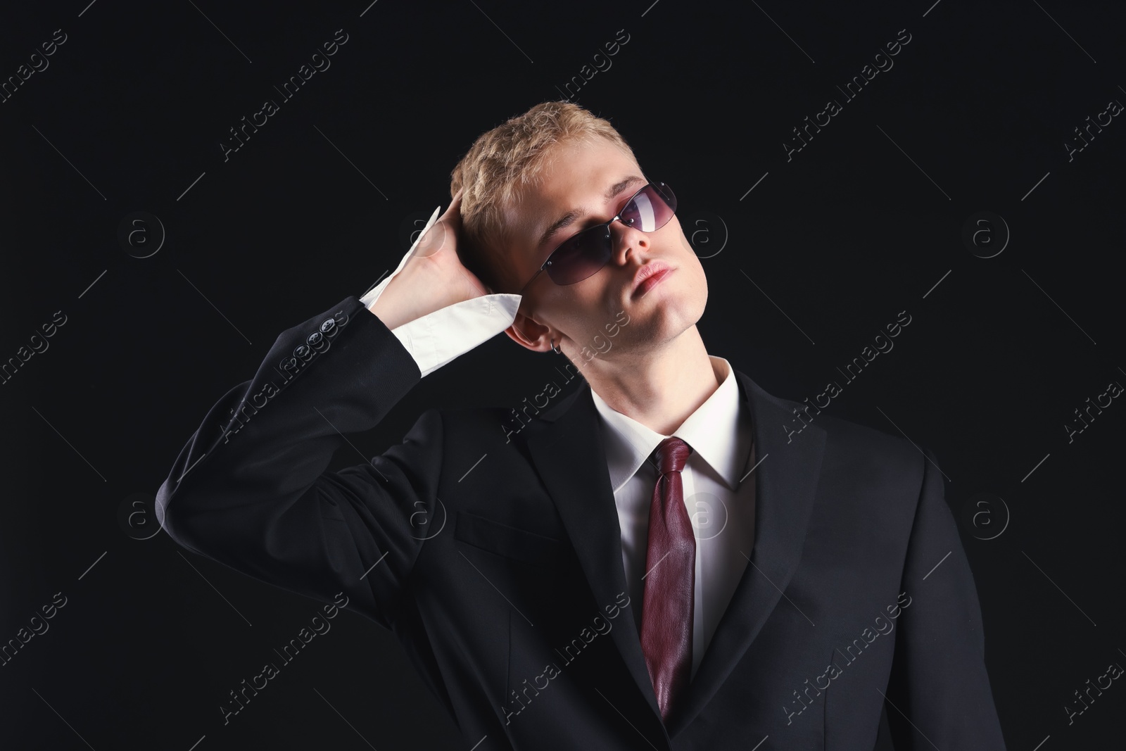 Photo of Handsome young man wearing stylish suit and sunglasses on black background