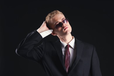 Photo of Handsome young man wearing stylish suit and sunglasses on black background