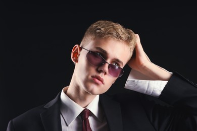 Photo of Handsome young man wearing stylish suit and sunglasses on black background