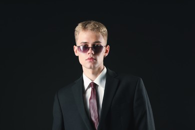 Photo of Handsome young man wearing stylish suit and sunglasses on black background