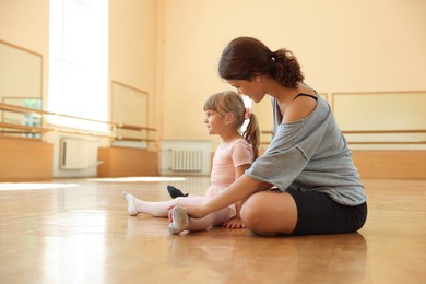 Photo of Ballet teacher working with little girl on floor in dance class