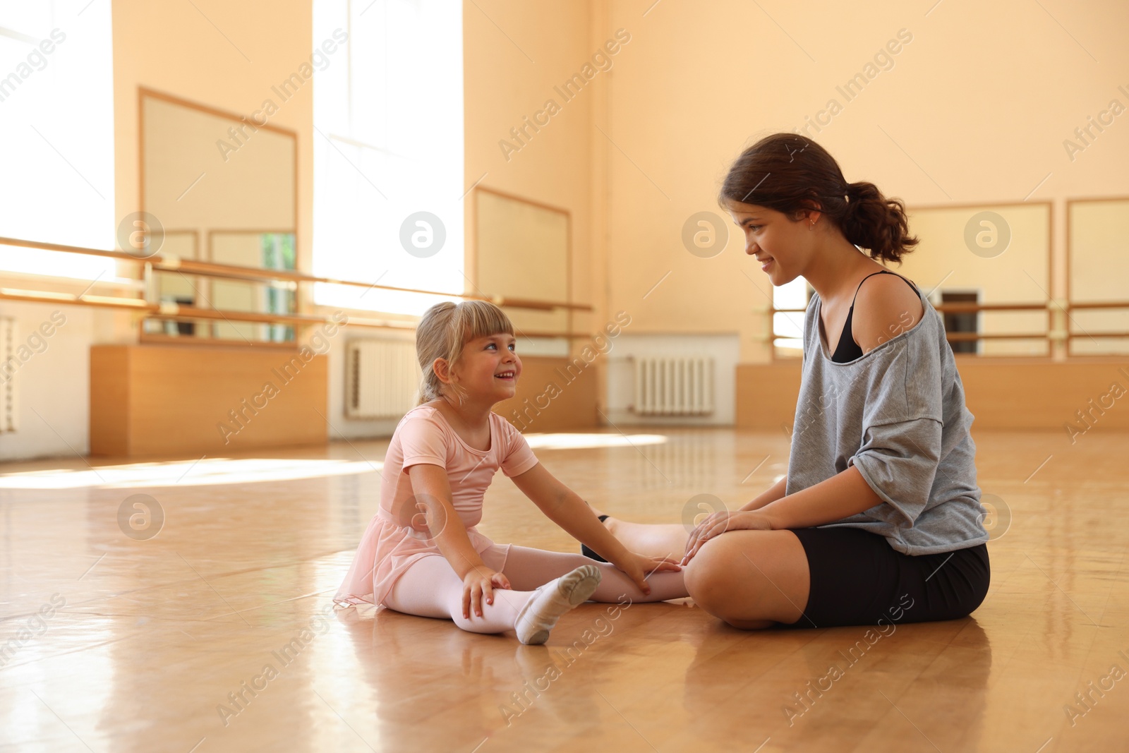 Photo of Happy ballet teacher working with little girl on floor in dance class