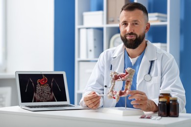 Photo of Gastroenterologist showing model of large intestine at white table in clinic