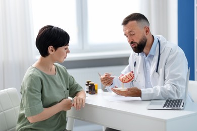 Photo of Gastroenterologist with model of stomach consulting woman in clinic