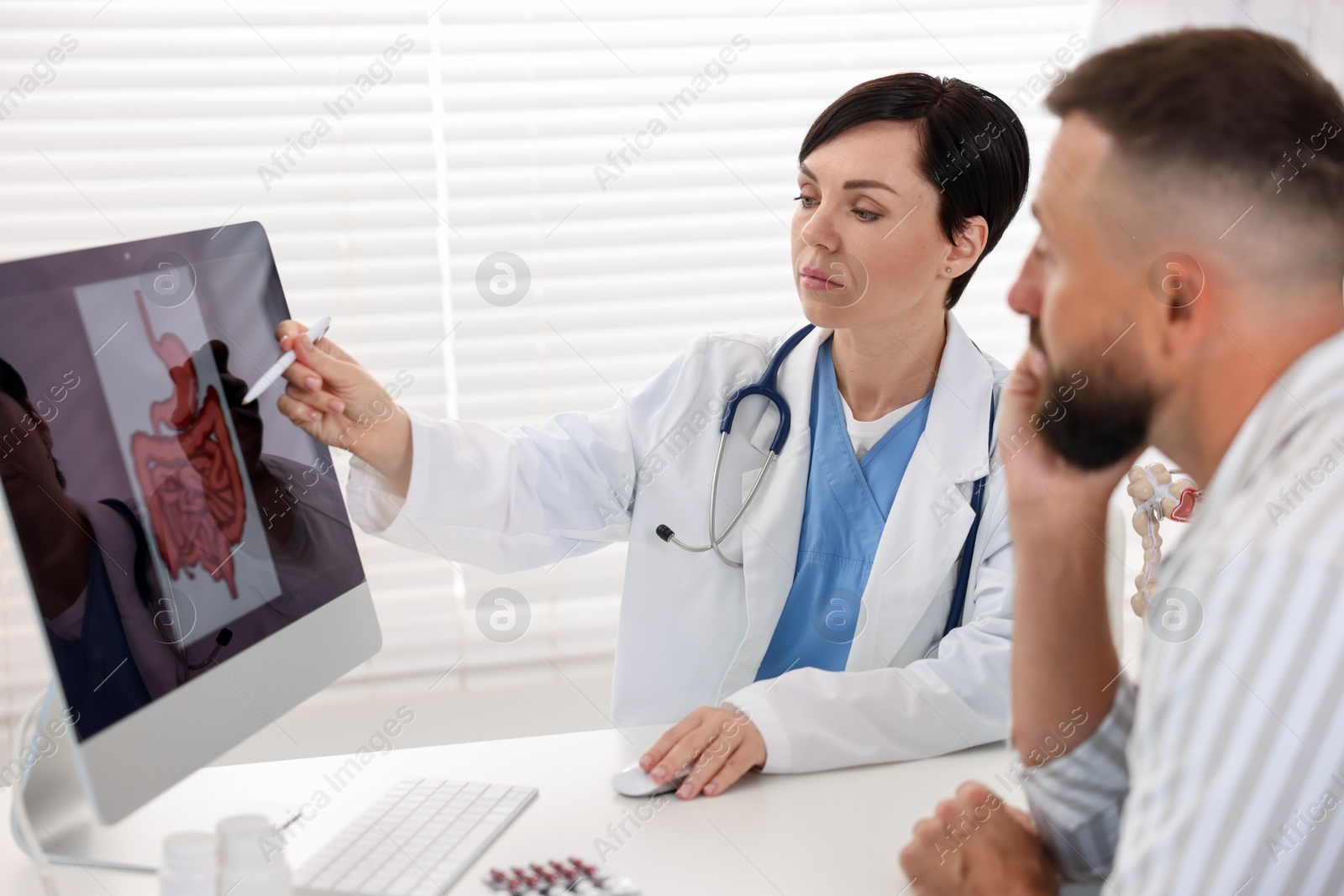 Photo of Gastroenterologist showing screen with illustration of digestive tract to patient at table in clinic