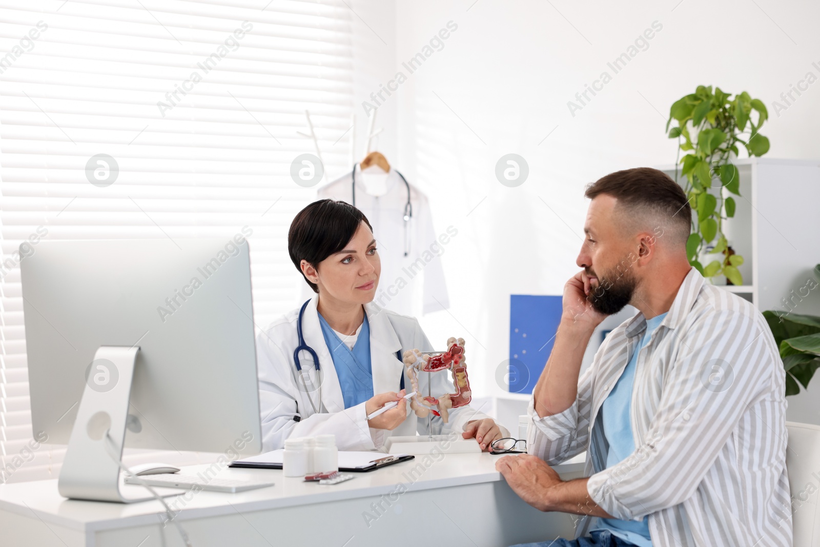 Photo of Gastroenterologist with model of large intestine consulting man in clinic
