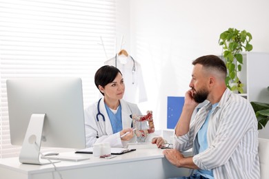 Photo of Gastroenterologist with model of large intestine consulting man in clinic