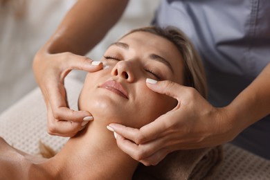 Photo of Beautiful woman receiving facial massage on couch in spa salon, closeup