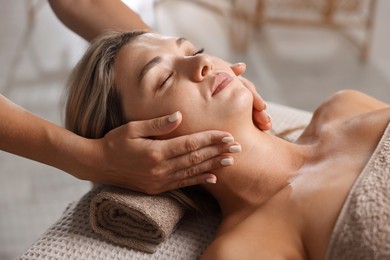 Photo of Beautiful woman receiving facial massage on couch in spa salon, closeup