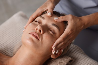 Photo of Beautiful woman receiving facial massage on couch indoors, closeup