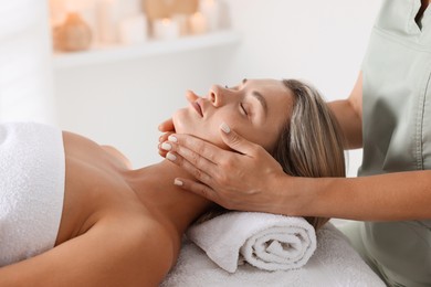 Photo of Beautiful woman receiving facial massage on couch in spa salon, closeup