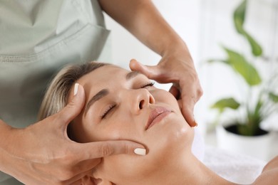 Photo of Beautiful woman receiving facial massage indoors, closeup