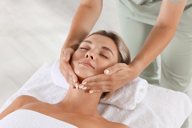 Photo of Beautiful woman receiving facial massage on couch indoors, closeup