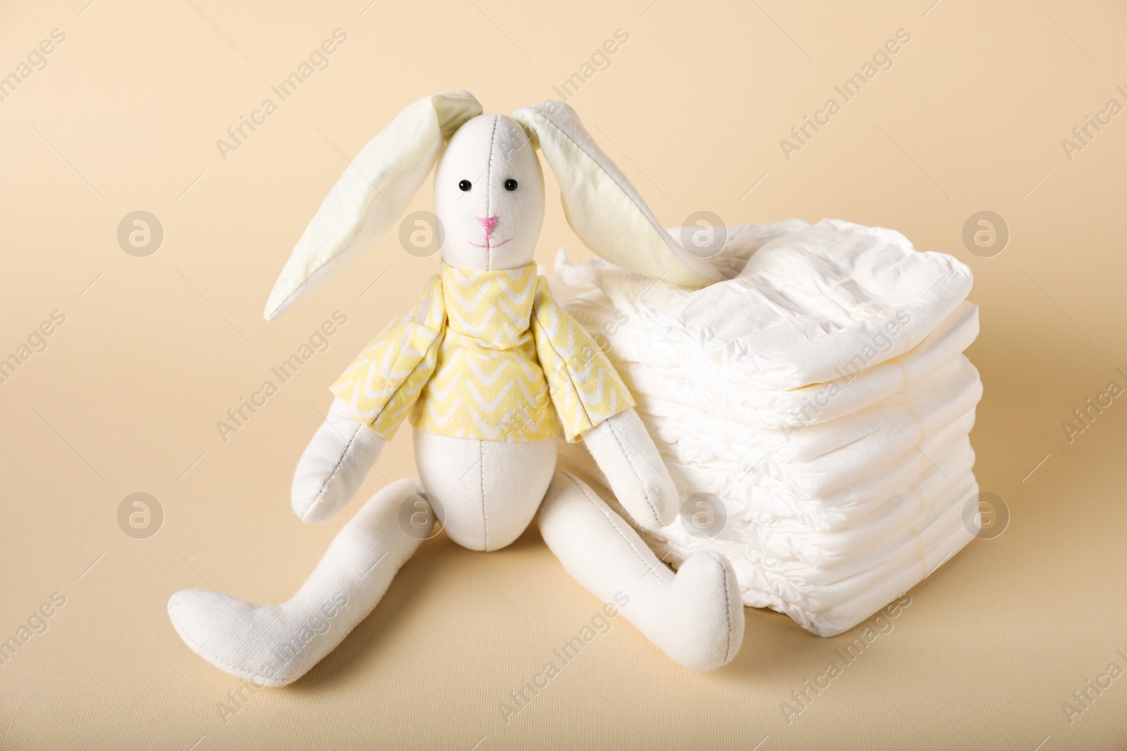 Toy bunny and diapers on beige background. Baby accessories Photo of Toy bunny and diapers on beige background. Baby accessories