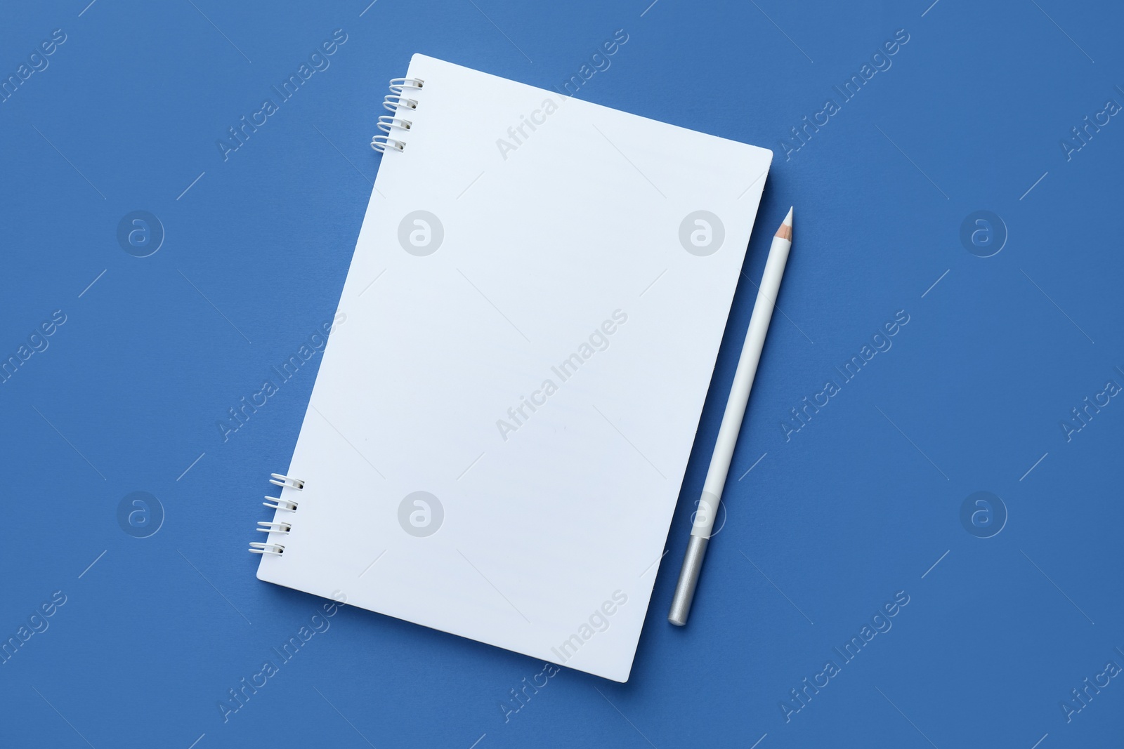 White notebook and pencil on blue background, top view. Space for text Photo of White notebook and pencil on blue background, top view. Space for text