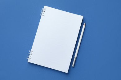 Photo of White notebook and pencil on blue background, top view. Space for text