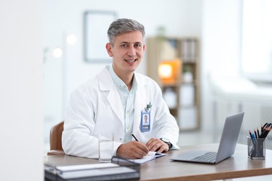Photo of Telemedicine. Doctor making notes while having video call with patient via laptop indoors