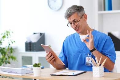 Photo of Telemedicine. Doctor showing okay gesture during video call with patient via tablet indoors
