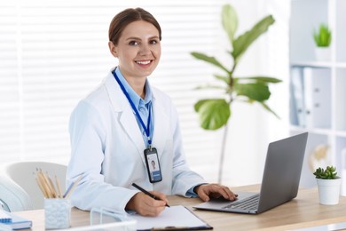 Photo of Telemedicine. Doctor making notes while having video call with patient via laptop indoors