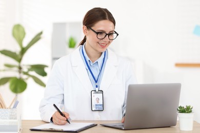 Photo of Telemedicine. Doctor making notes while having video call with patient via laptop indoors