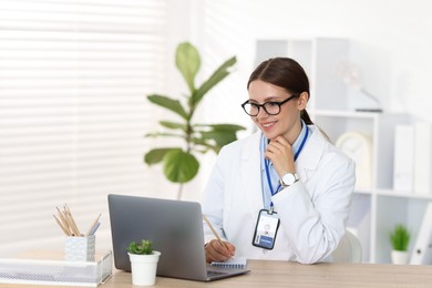Photo of Telemedicine. Doctor making notes while having video call with patient via laptop indoors
