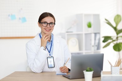 Photo of Telemedicine. Doctor making notes while having video call with patient via laptop indoors