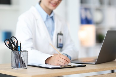 Photo of Telemedicine. Doctor making notes while having video call with patient via laptop indoors, closeup