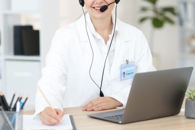 Photo of Telemedicine. Doctor making notes while having video call with patient via laptop indoors, closeup