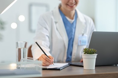 Photo of Telemedicine. Doctor making notes while having video call with patient via laptop indoors, closeup