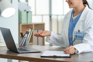 Photo of Telemedicine. Doctor making notes while having video call with patient via laptop indoors, closeup