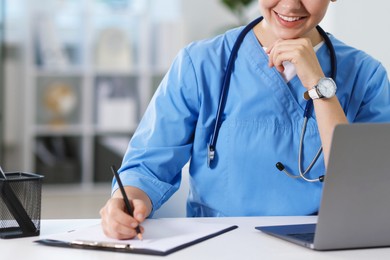 Photo of Telemedicine. Doctor making notes while having video call with patient via laptop indoors, closeup