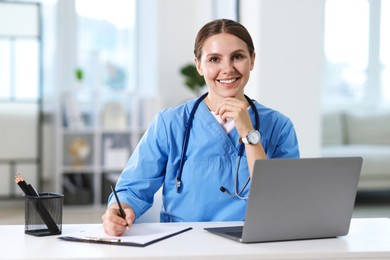Photo of Telemedicine. Doctor making notes while having video call with patient via laptop indoors