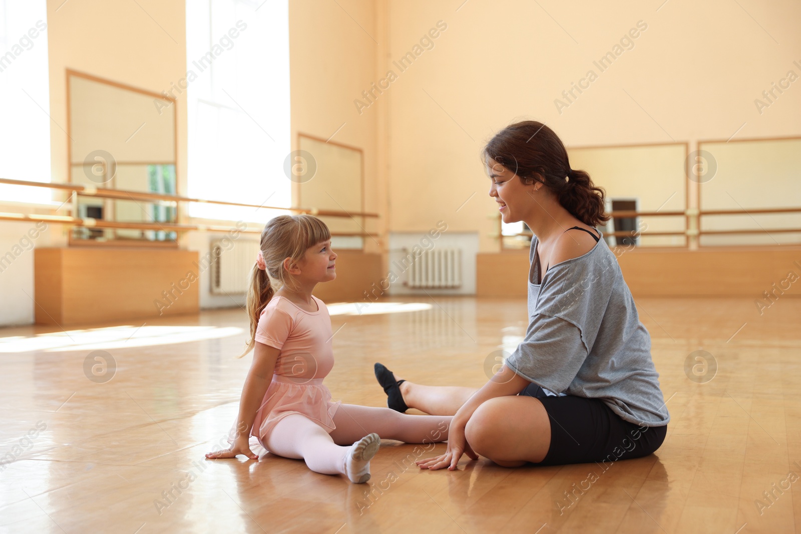 Photo of Ballet teacher working with little girl on floor in dance class