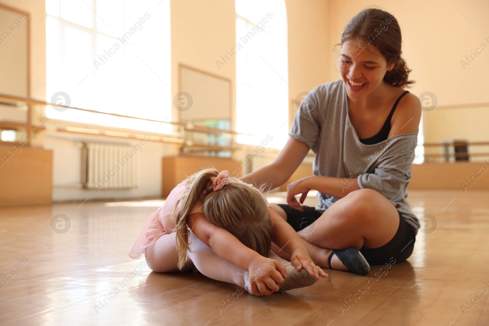 Smiling ballet teacher helping little girl to stretch in dance class Photo of Smiling ballet teacher helping little girl to stretch in dance class