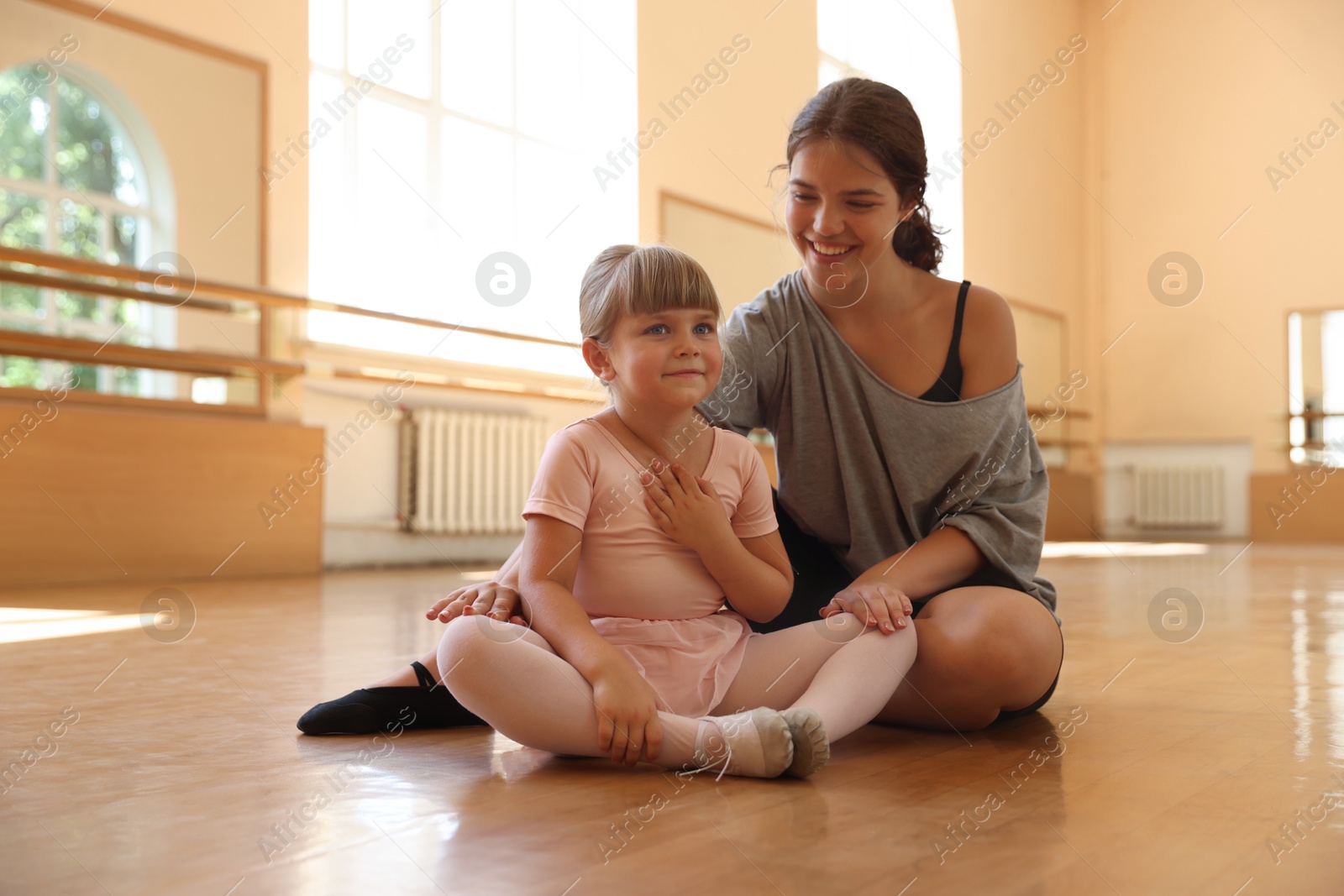 Photo of Happy ballet teacher working with little girl on floor in dance class